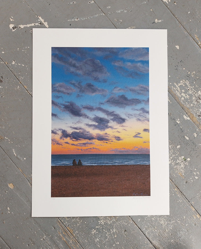 Art print of a sunset over Brighton beach with two people sitting on the pebbles.