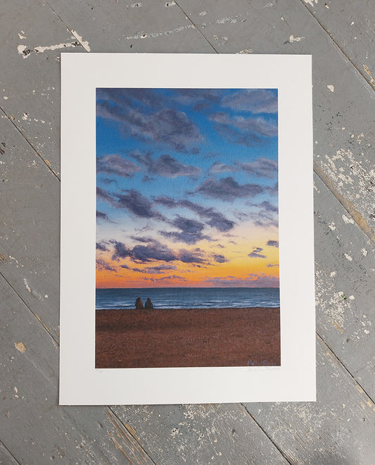 Art print of a sunset over Brighton beach with two people sitting on the pebbles.
