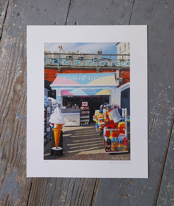 Art print of a colorful ice cream shop in Brighton with an ice cream cone on a wooden surface.