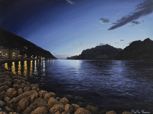 Painting by artist Martin Thomas of Lake Garda in Italy at night with illuminated buildings and rocky shore. Original artwork of acrylic paint on canvas