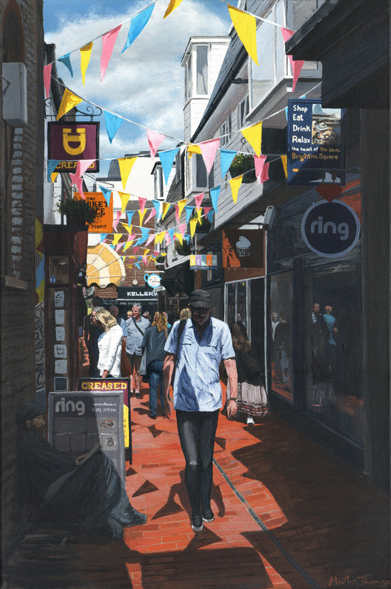 Painting by Martin Thomas of a narrow street in The Lanes with people walking, colorful flags, and shopfronts